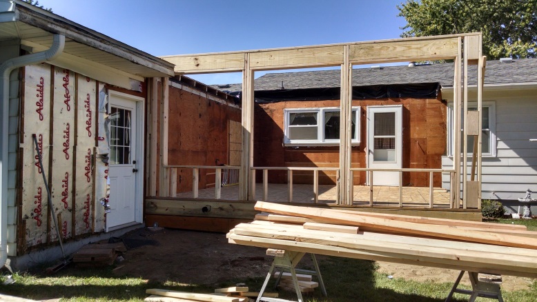 Wooden framing for a home addition under construction, with lumber stacked on sawhorses.