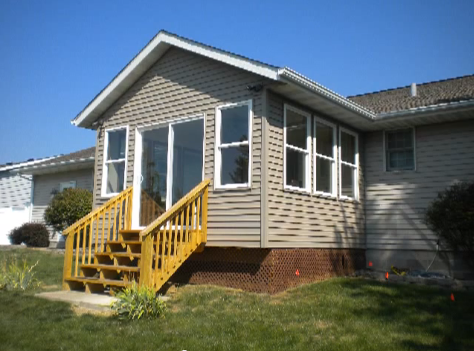 Sunroom addition with tan siding, large windows, and wooden entry stairs.
